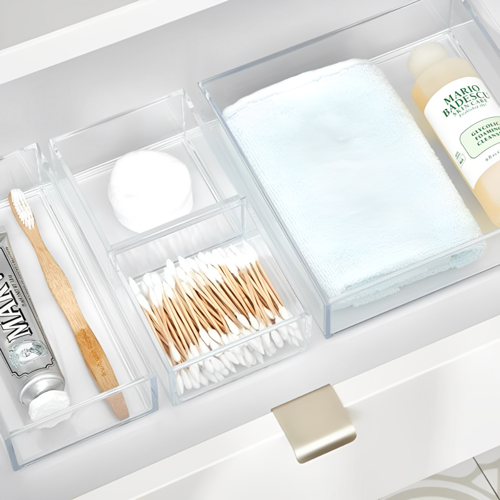 Eine Badezimmerschublade ist mit Bambuszahnbürste, Zahnpasta, Wattekugeln und Mario Badescu Reinigungsgel in klaren Acrylschalen aus dem iDesign Schubladen Organizer-Set CLARITY (5-teilig) übersichtlich geordnet.