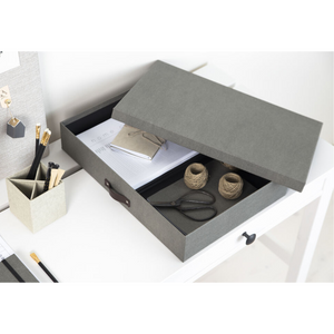 Eine graue Bigso SVERKER Aufbewahrungsbox A3 aus Canvas steht mit halb geöffnetem Deckel auf einem weißen Schreibtisch. Im Inneren: Notizbücher, Schnur und Schere-ideal zur Dokumentenaufbewahrung im organisierten Arbeitsbereich.