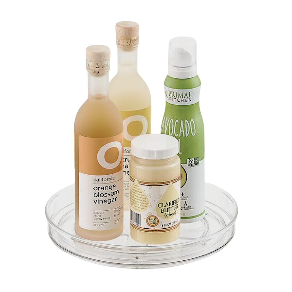 Die iDesign HOME EDIT - Drehteller Lazy Susan KLAR (23x3,5cm) zeigt zwei Flaschen Essig, eine Dose Avocado-Spray und ein Glas Butterschmalz vor einem schlichten weißen Hintergrund.