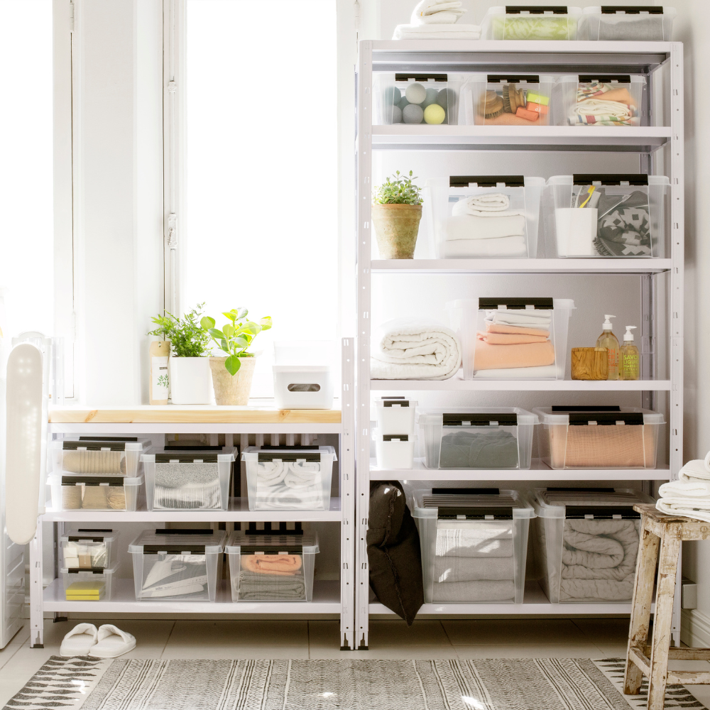 Offene Regale und ein Tisch am Fenster sind mit der Orthex SmartStore Box KLAR - 50x39x26cm (31L) ordentlich organisiert. Topfpflanzen sorgen für Charme, während das Sonnenlicht diesen hellen, aufgeräumten Raum erfüllt.