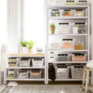 Offene Regale und ein Tisch am Fenster sind mit der Orthex SmartStore Box KLAR - 50x39x26cm (31L) ordentlich organisiert. Topfpflanzen sorgen für Charme, während das Sonnenlicht diesen hellen, aufgeräumten Raum erfüllt.