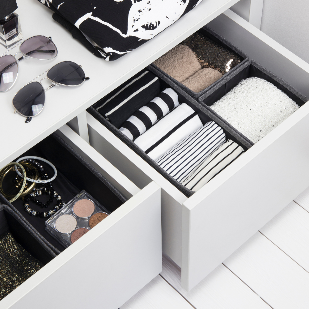 Schubladen mit Kleidung, Accessoires und Brillenetui, daneben Sonnenbrille und Nagellack auf weißer Fläche.