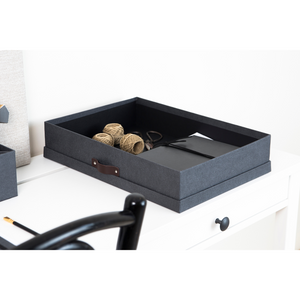 Eine SVERKER Aufbewahrungsbox A3 in Schwarz Canvas von Bigso steht auf einem weißen Schreibtisch, auf dem Garnrollen, Scheren und Notizbücher ordentlich aufbewahrt werden. Ein schwarzer Stuhl und ein Bleistift vervollständigen die minimalistische, organisierte Szene.