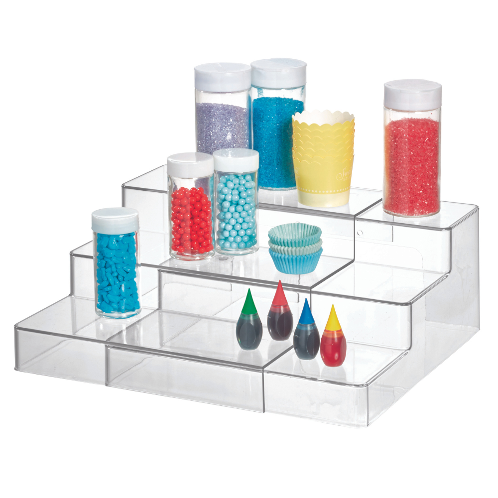 Das ausziehbare HOME EDIT Küchen- und Gewürzregal KLAR von iDesign präsentiert bunte Streuselgläser, Cupcake-Förmchen und vier Lebensmittelfarben (grün, rot, schwarz, gelb) übersichtlich auf weißem Hintergrund.