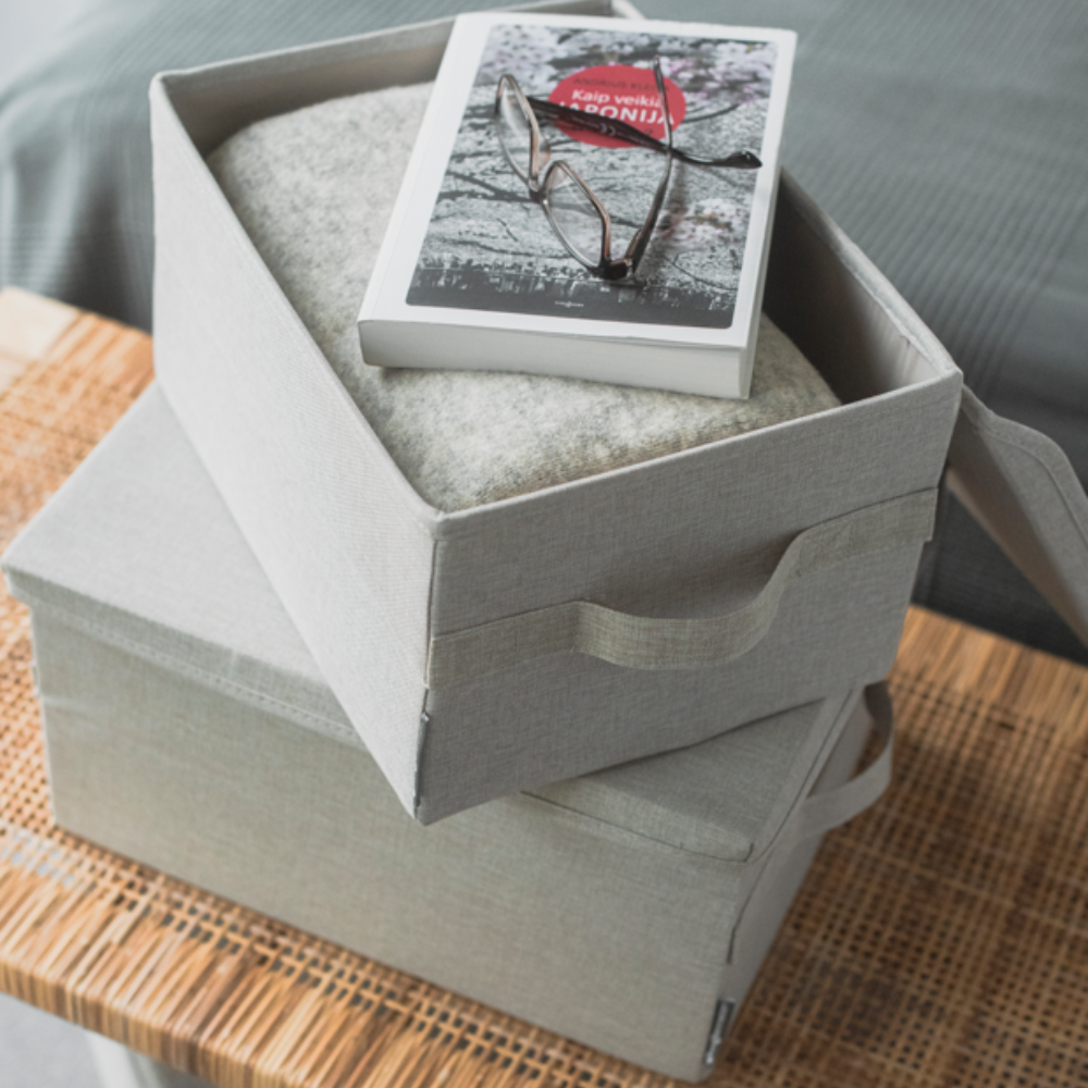 Zwei Bigso SOFT Aufbewahrungsboxen in Beige (40x30x22cm) stehen übereinander auf einer geflochtenen Oberfläche. Die obere Box ist geöffnet, darin liegen eine Decke, ein Buch und eine Brille.
