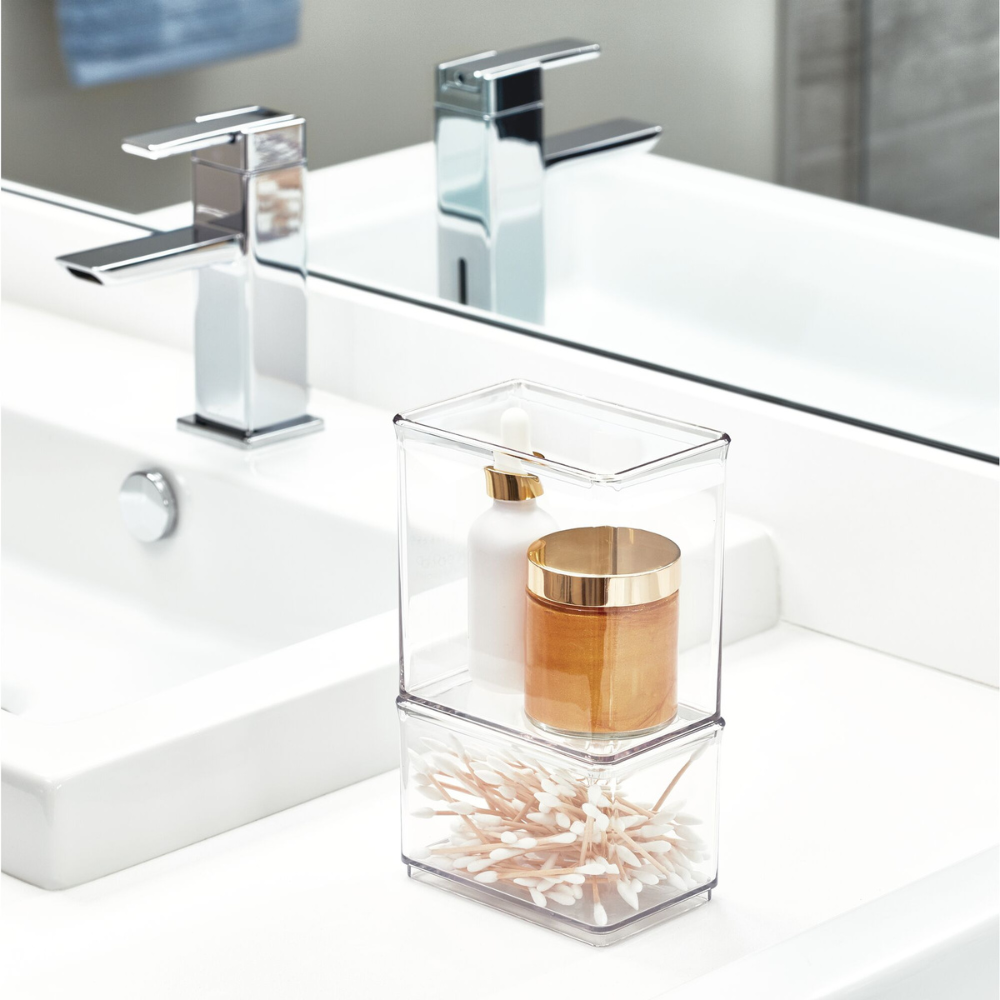Two transparent boxes with cotton swabs and care products on a washbasin with fittings.